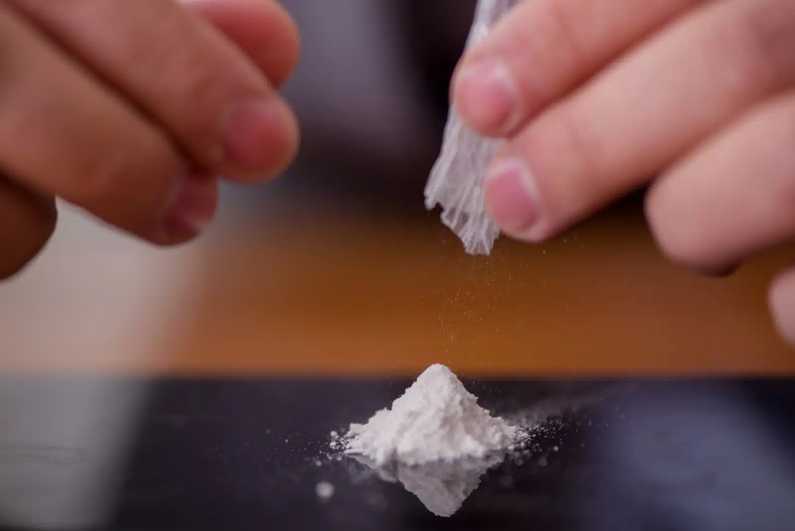 Substance Use vs. Abuse: A flat surface with a small pile of white powder. Over the powder are two hands, one holding rolled plastic.