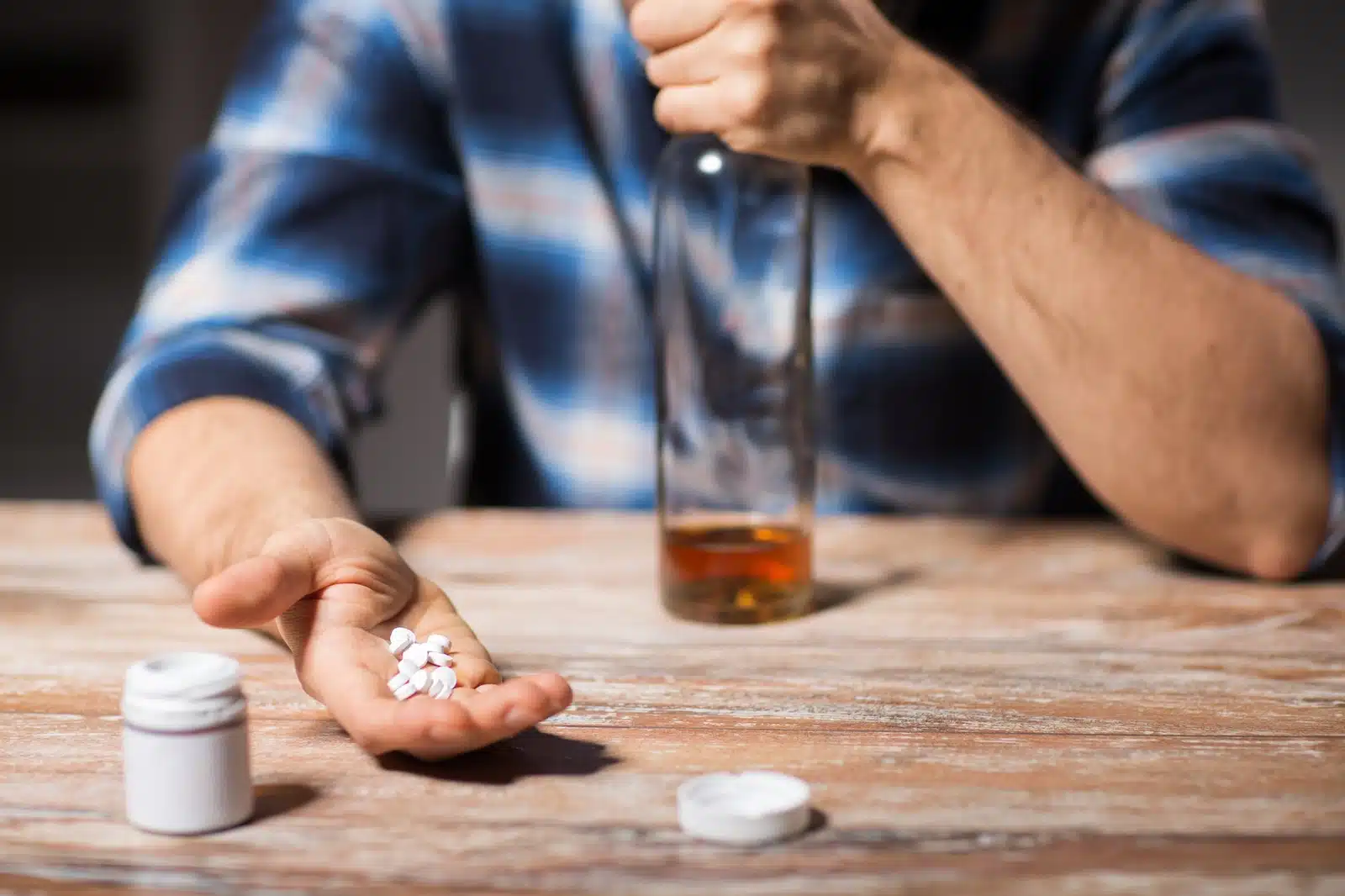 When Does Substance Use Become a Problem? A man holding several pills in one hand, and a mostly empty bottle of alcohol in the other.