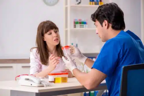 Drug Testing In The Workplace: A nurse handing a urine sample cup to a woman.