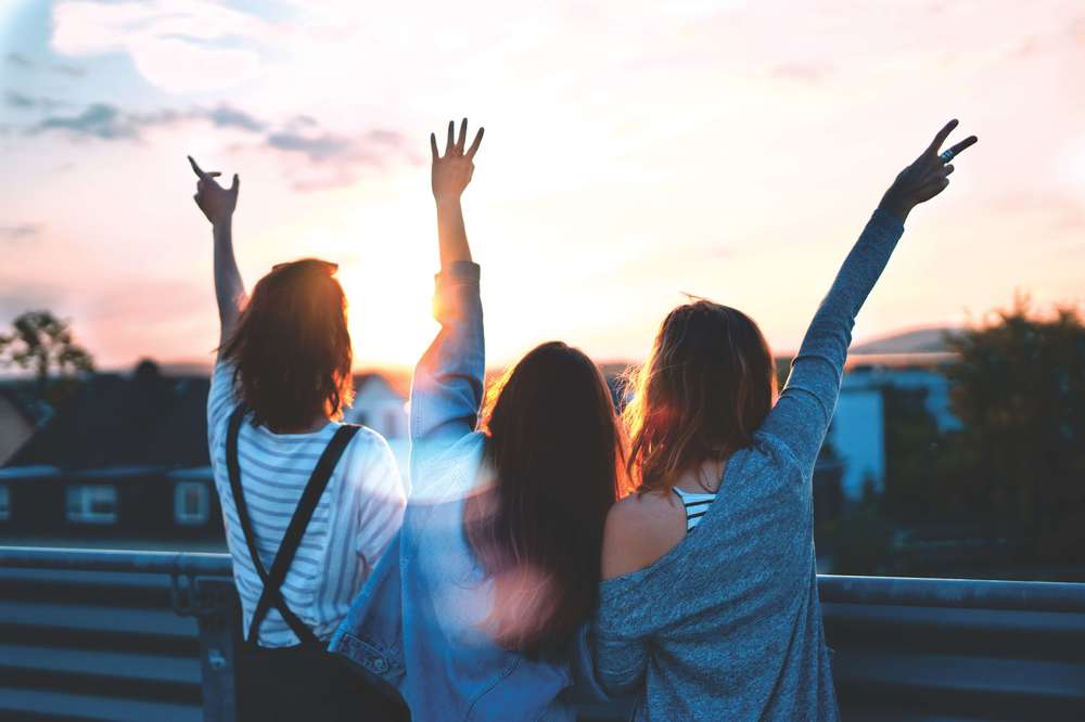 Recovering alcoholic women cheering women open arms at sunset mountain top cliff edge