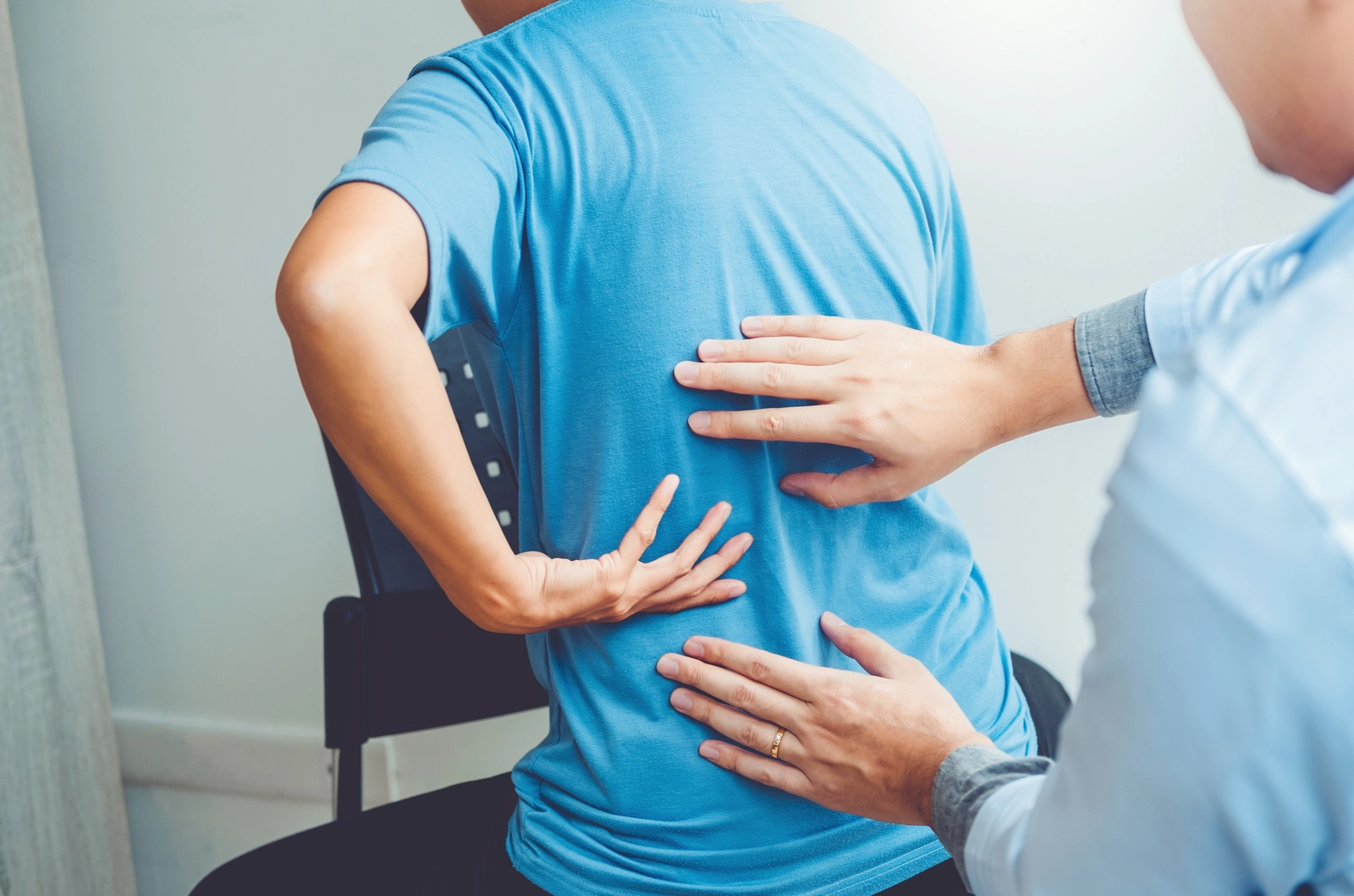 man with back pain is examined by health care professional